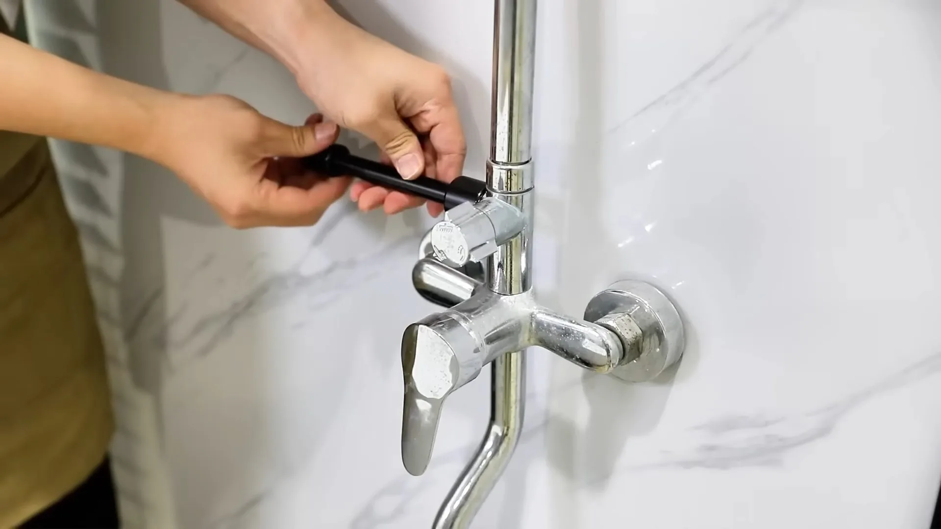 Two hands adjusting a chrome wall-mounted tub and shower faucet set into marble tile.