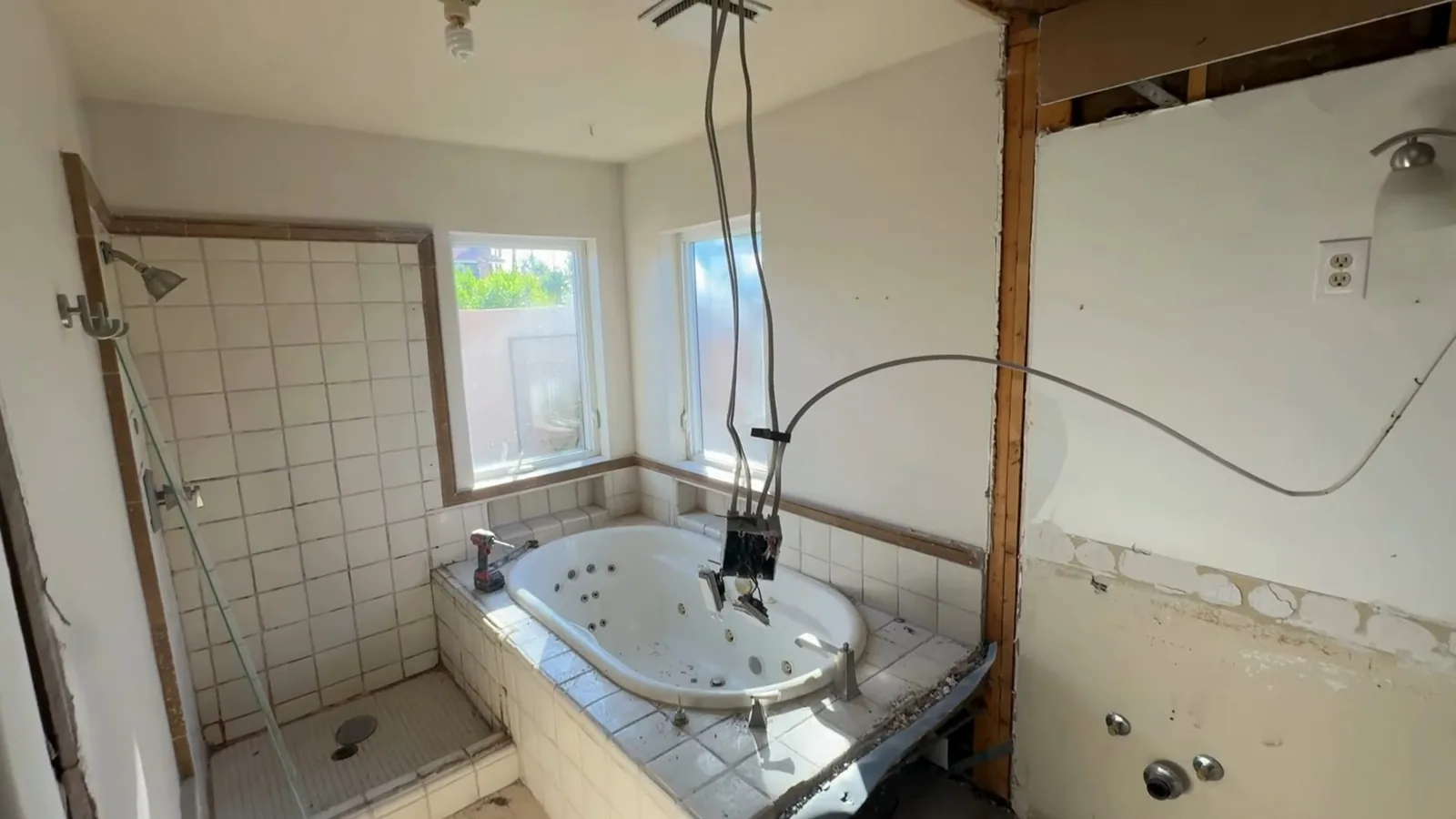 A bathroom in demolition with open walls, a tiled shower and a jetted tub still in place.