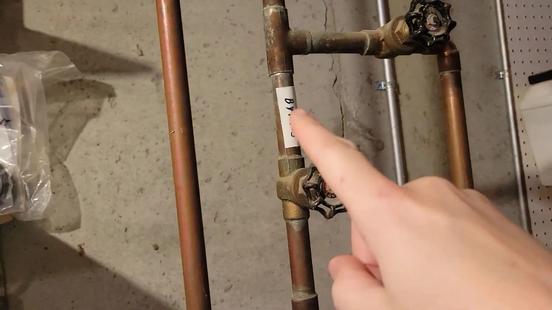 A finger pointing at a gate valve on copper pipes in a basement.