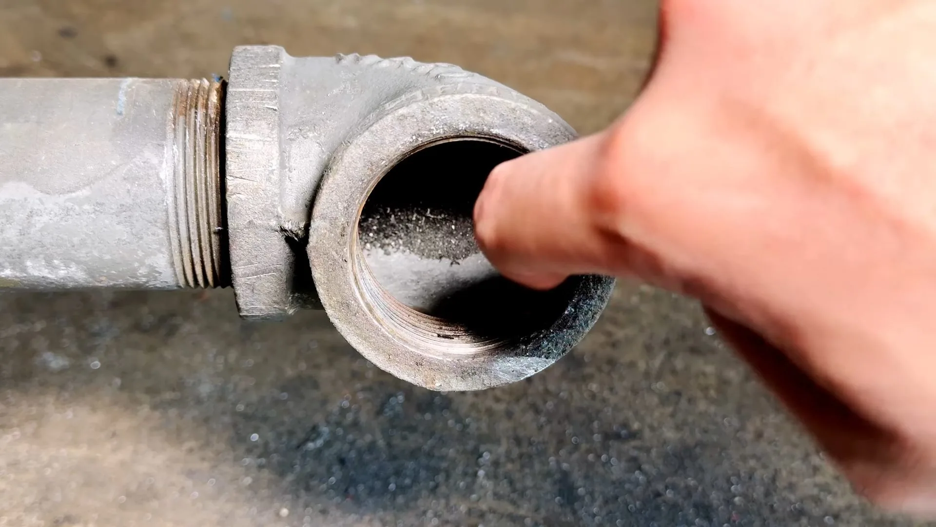 A finger pointing into an open galvanized cast-iron cleanout fitting.