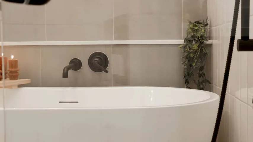 A freestanding bathtub beside a dark wall-mounted spout and two valve handles.