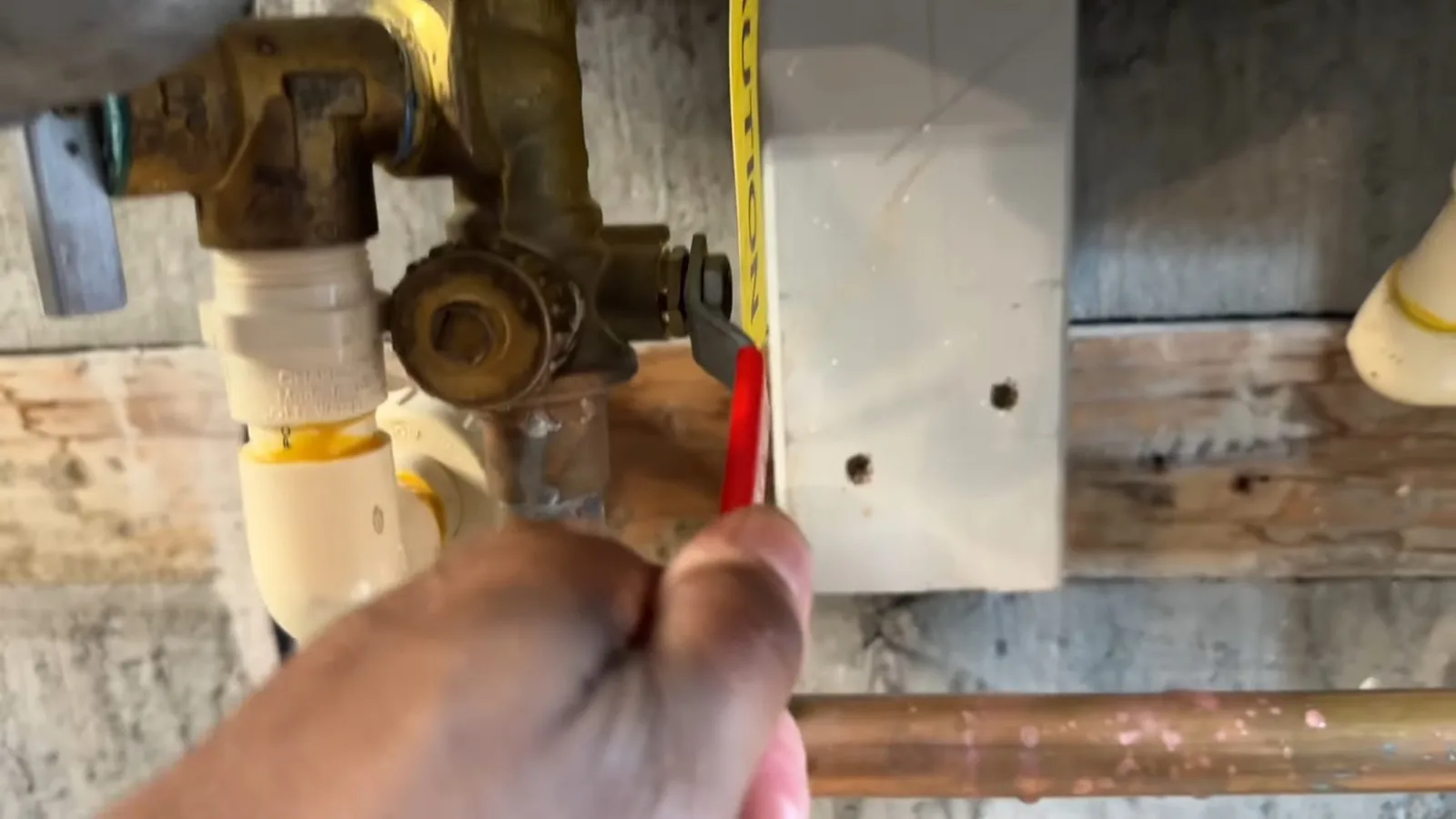 A hand holding a tape measure beside brass service valves on a wall.
