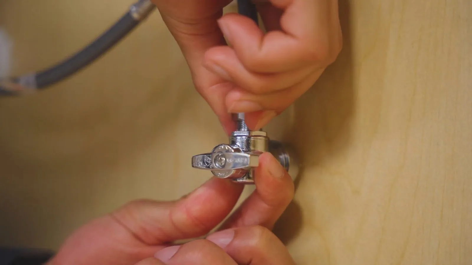 Two hands connecting a quarter-turn supply stop valve to a water line.