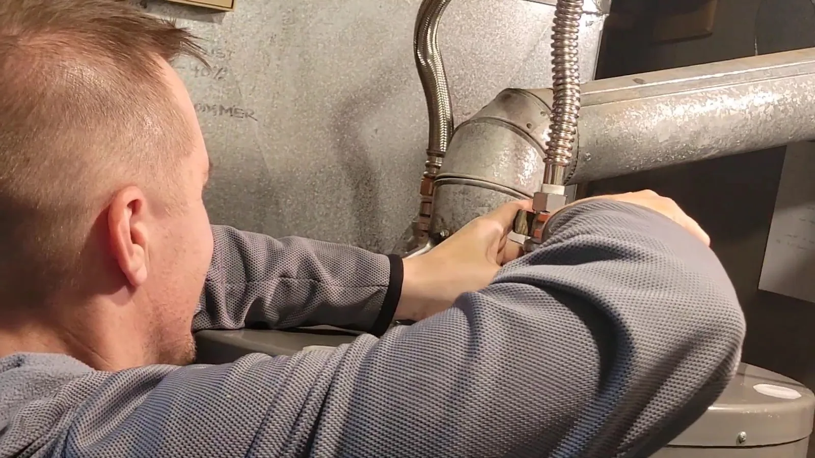 A man leaning in to connect a flexible line at the top of a water heater.