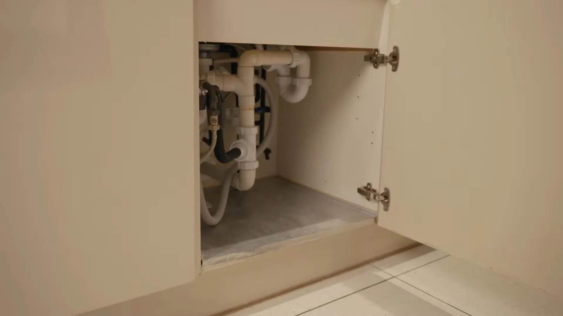 The inside of an open sink cabinet showing white drain pipes, two supply lines and a P-trap.