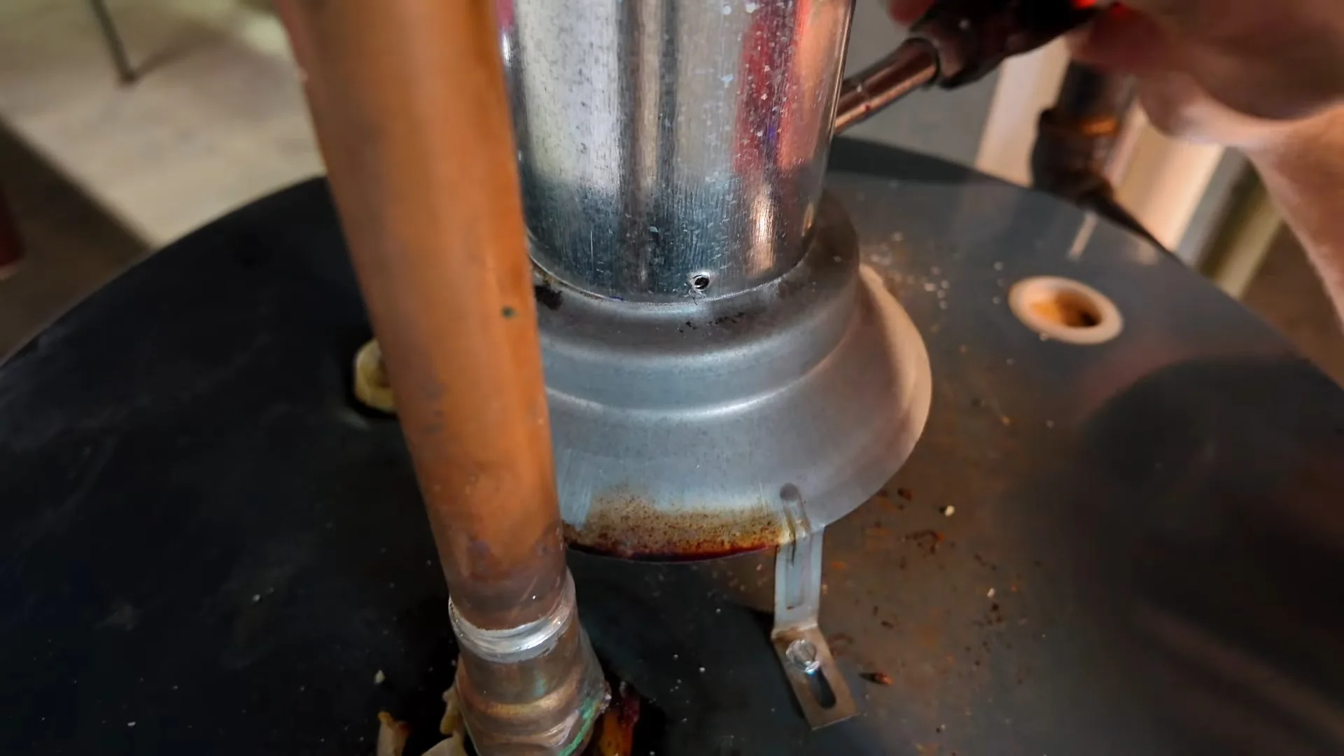 Copper pipe and a galvanized flue collar with rust on the black top of a water heater tank.