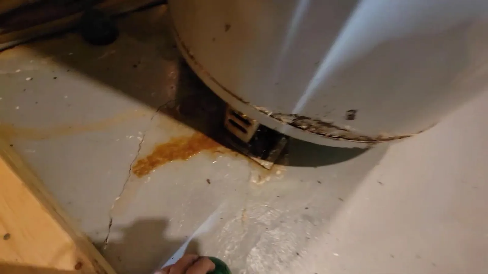 Rust-colored staining and water streaks on the floor under the base of a water heater tank.
