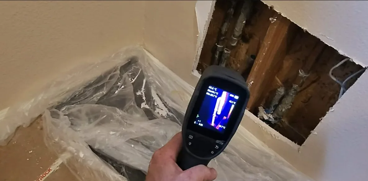 A thermal camera aimed at an opening in drywall with plastic sheeting hung around it.