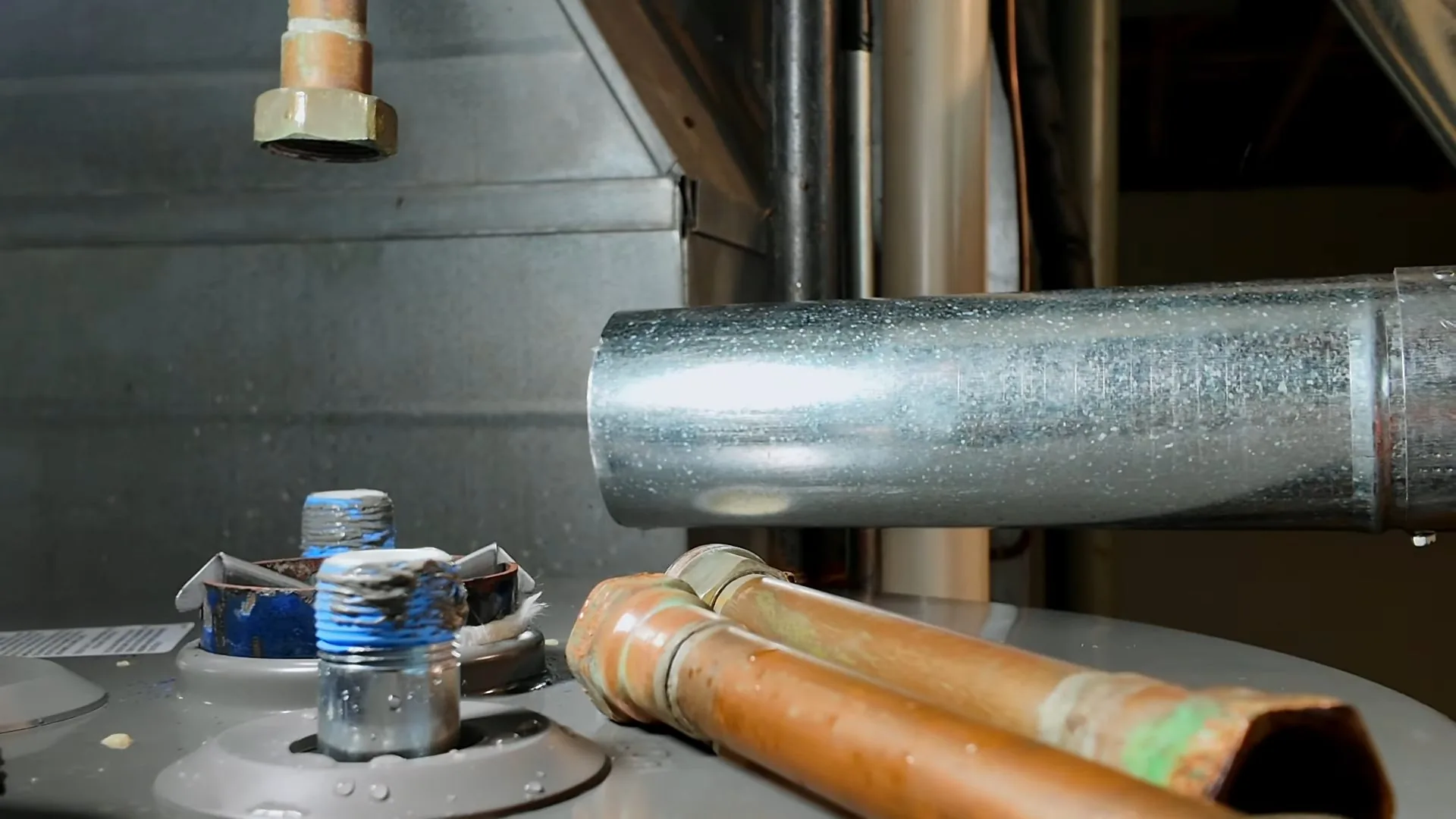 The top of a tank water heater with two copper supply lines, threaded connections and a galvanized vent pipe running off to the side.