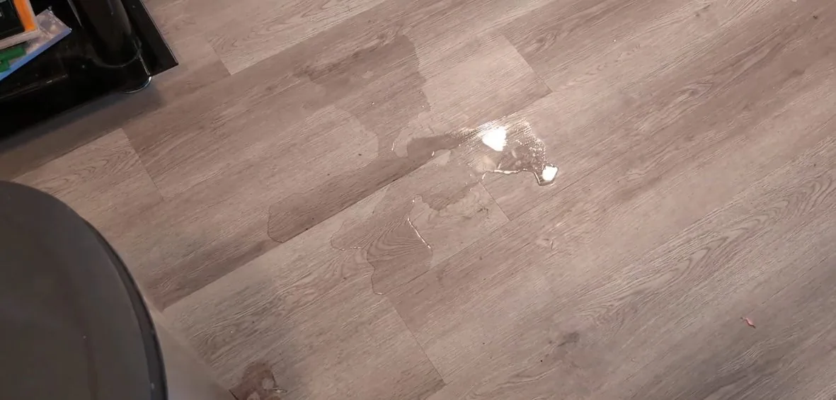 A wet laminate floor with a single water drop on its surface.
